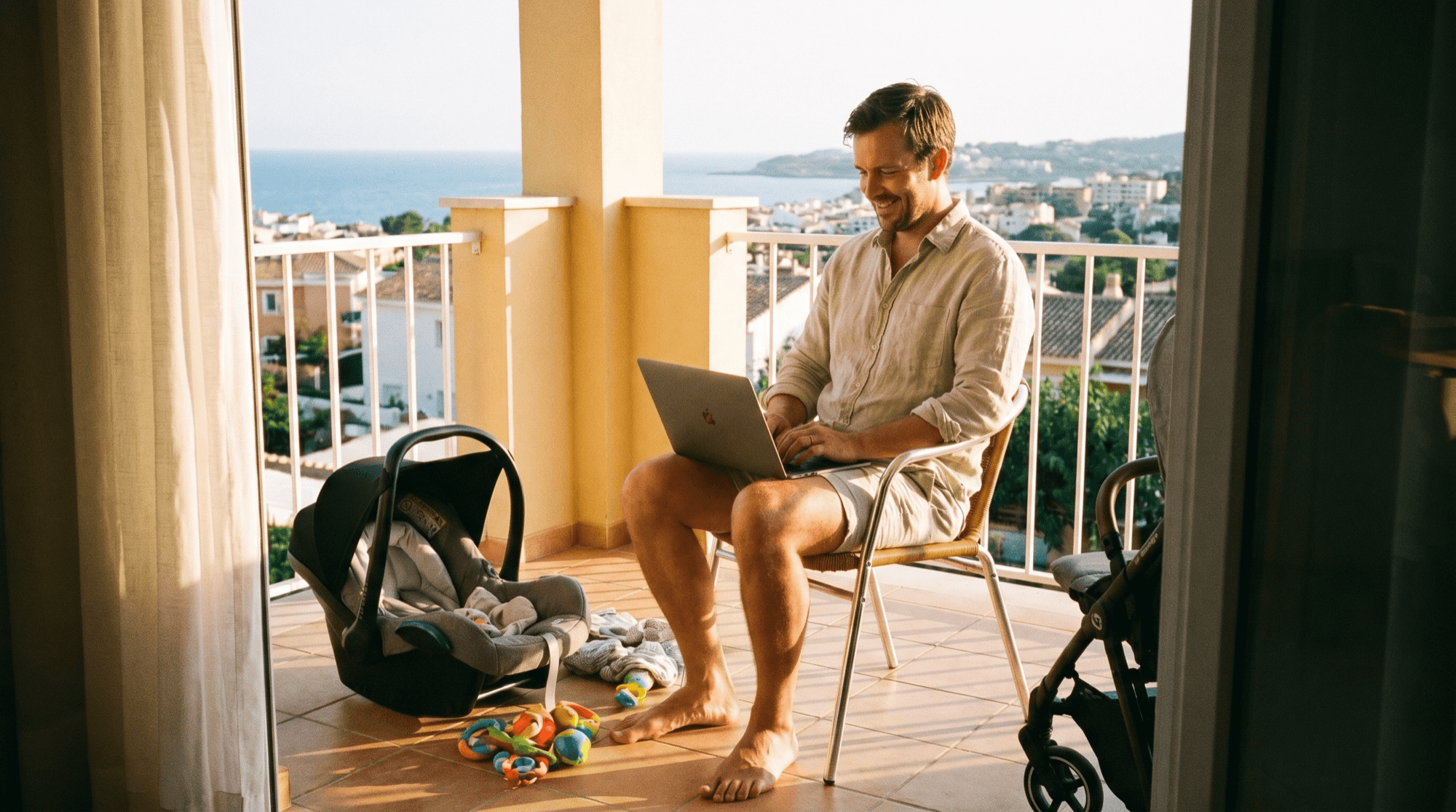 Far jobber på laptop på en solfylt balkong med babyutstyr i nærheten